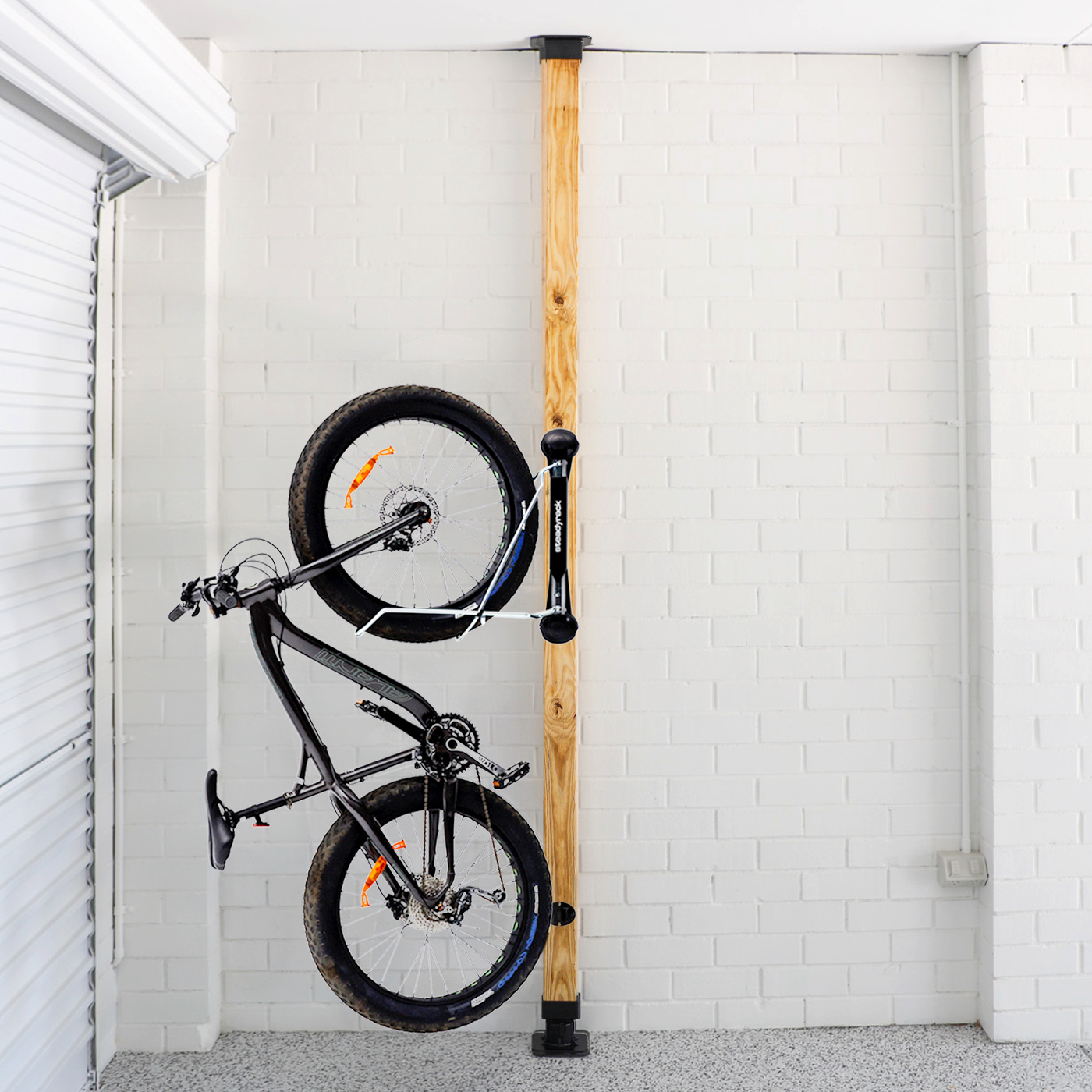 Bicycle mounted against a wooden post with white brick walls.