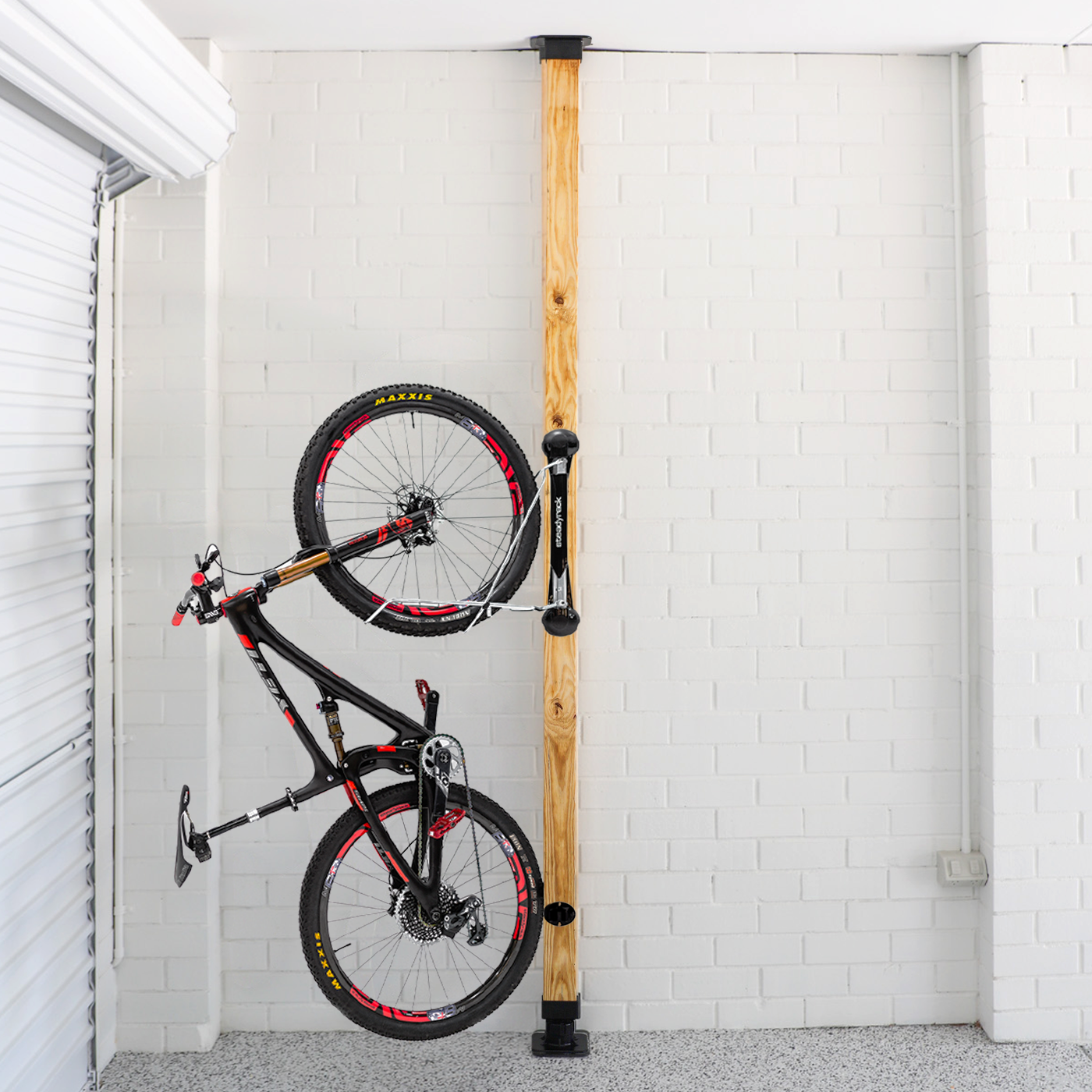 Bicycle mounted against a wooden post with white brick walls.