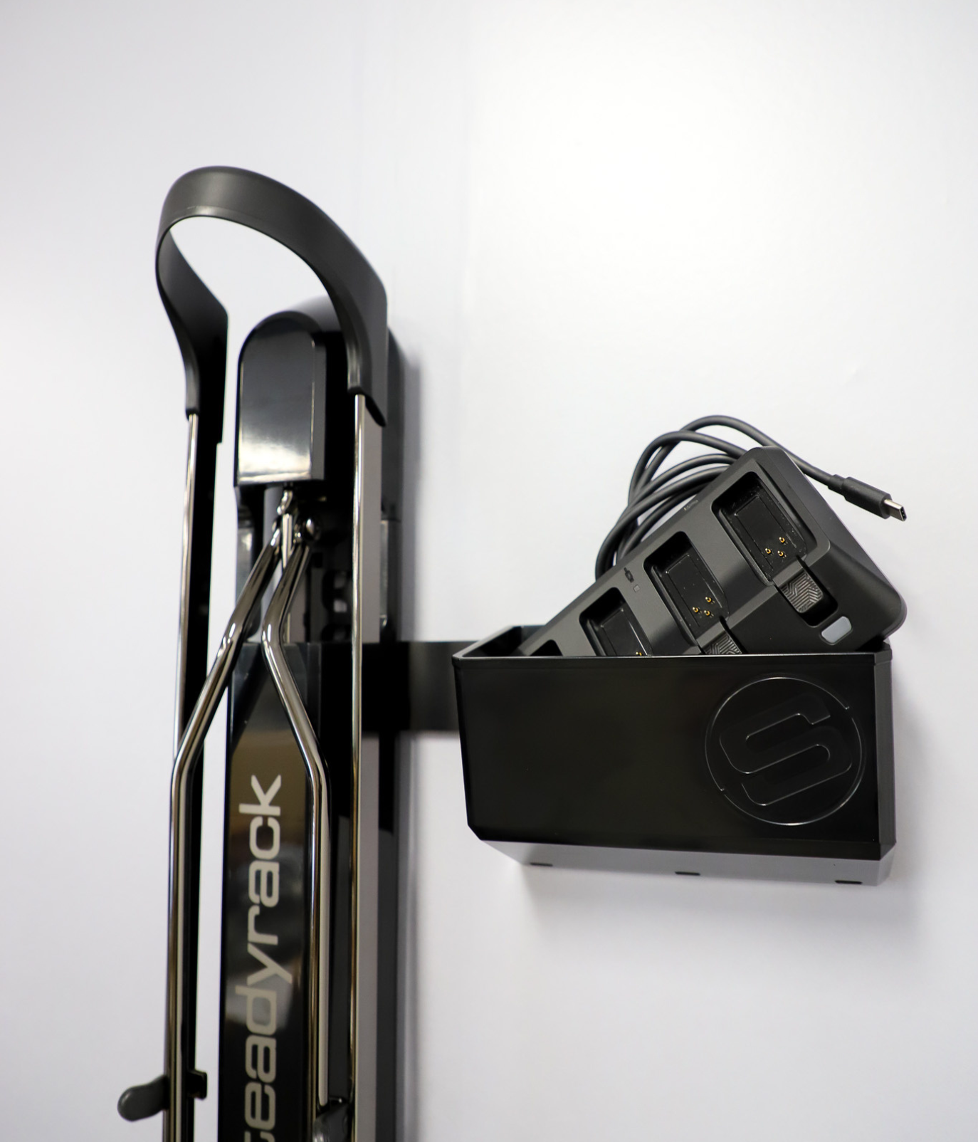 A black small compartment with a Steadyrack logo storing an eBike charger, connected to a bike rack with a bracket.