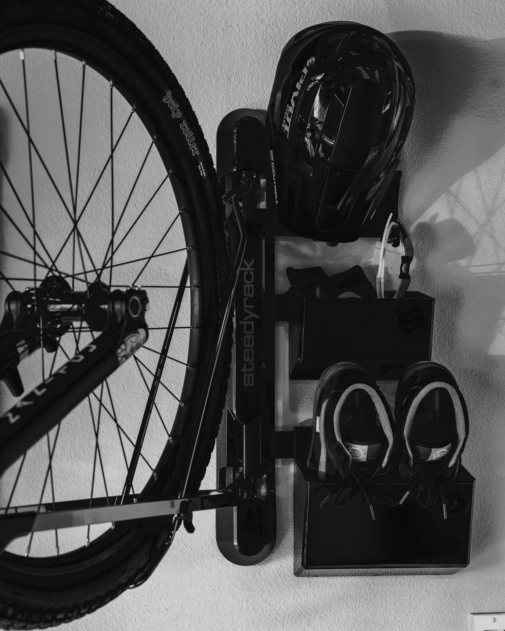 Bicycle in rack on a wall with shoes and a helmet on a holder.