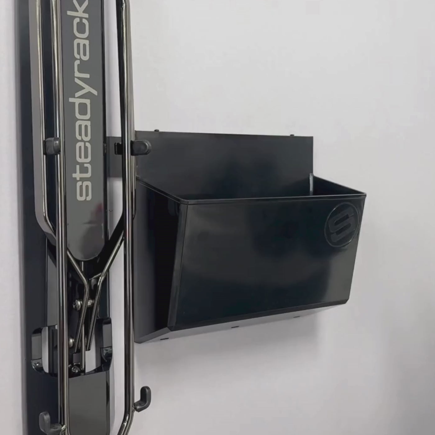 A person placing a pair of cycling shoes into a GearMate Large SteadyBin attached with a bracket to a bike rack. 